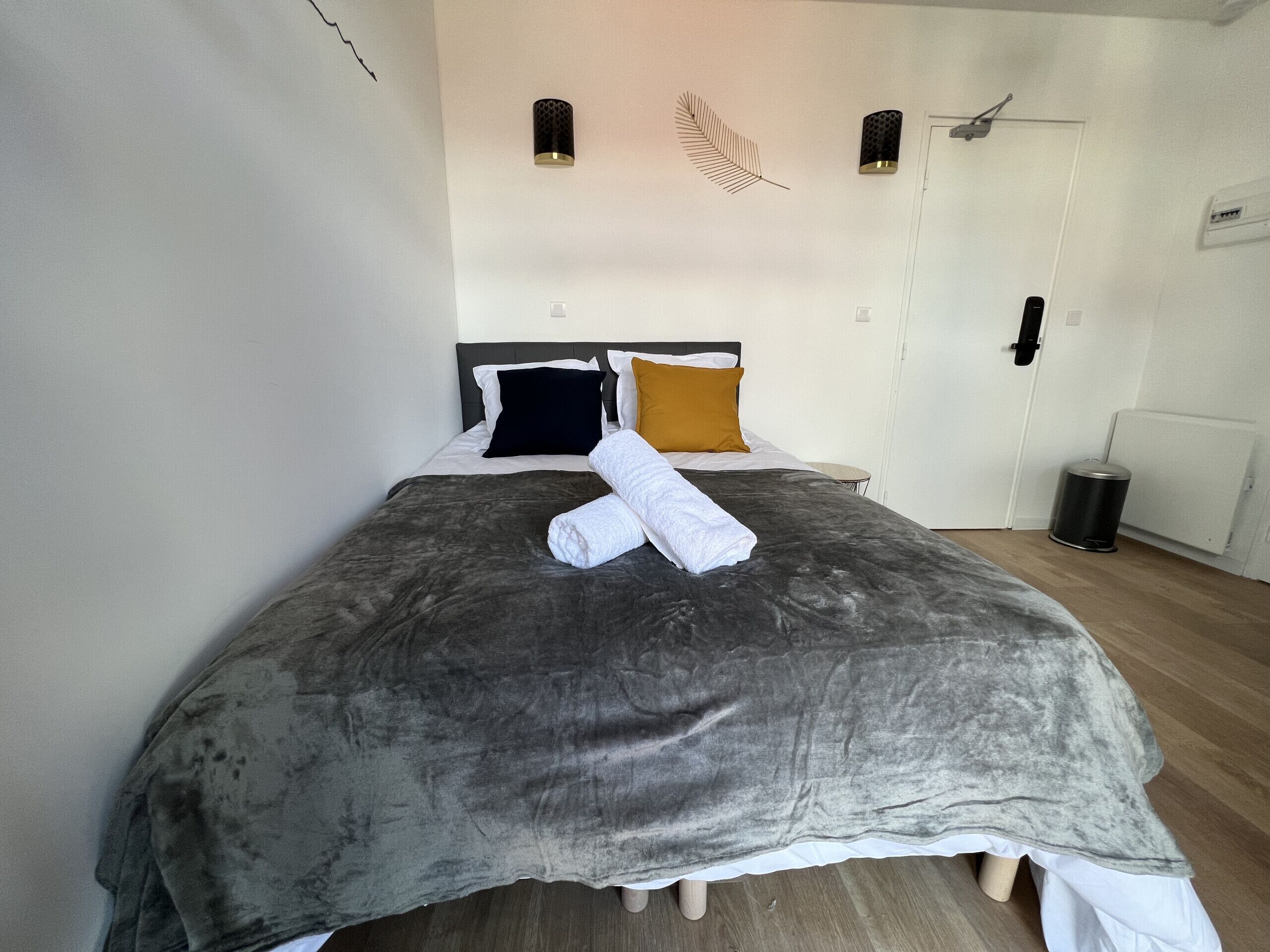 A neatly made bed with a grey duvet, two pillows, and a rolled white towel.