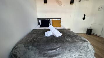 A neatly made bed with a grey duvet, two pillows, and a rolled white towel.