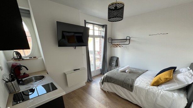 A modern bedroom with a bed, bedside table, and a TV mounted on the wall. - Vue sur les Toits - 2p downtown Liévin (Liévin)