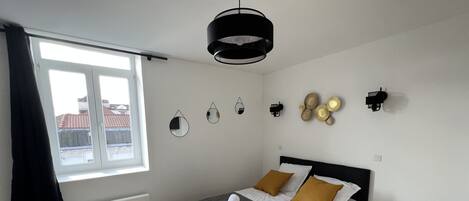 Un dormitorio con cama, ventana, radiador, lámpara colgante y adornos en la pared.