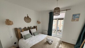 Une chambre à coucher avec un lit, une fenêtre avec des rideaux, une vue sur des immeubles et un luminaire fixé au mur.