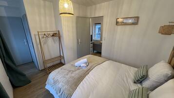 A bedroom with a bed, a hanging light fixture, a wooden coat rack, and a door leading to another room.