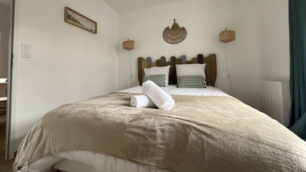 Un lit bien fait, avec une couette et des oreillers de couleur beige, une tête de lit en bois et une petite lampe fixée au mur.