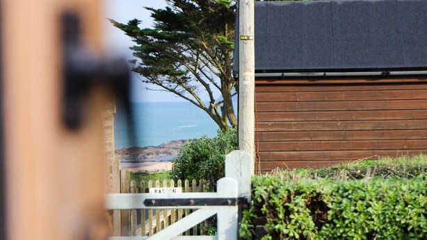 A wooden gate with a sign reading "RAISON" leading to a building with a brown exterior and a view of the ocean. - Beachside holiday home  (Padstow)