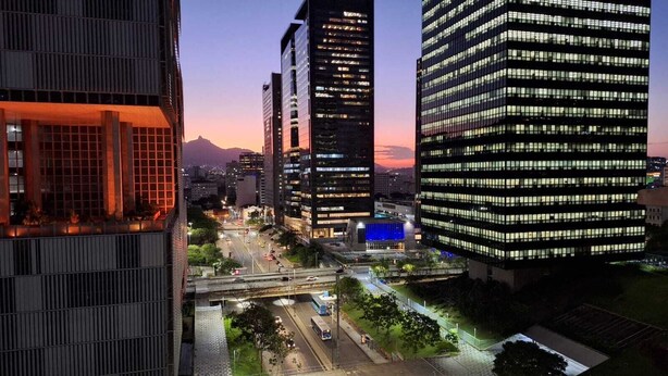 A cityscape at dusk with modern high-rise buildings, a busy street, and an overpass. - Seu aconchegante lar no centro carioca (Rio de Janeiro)