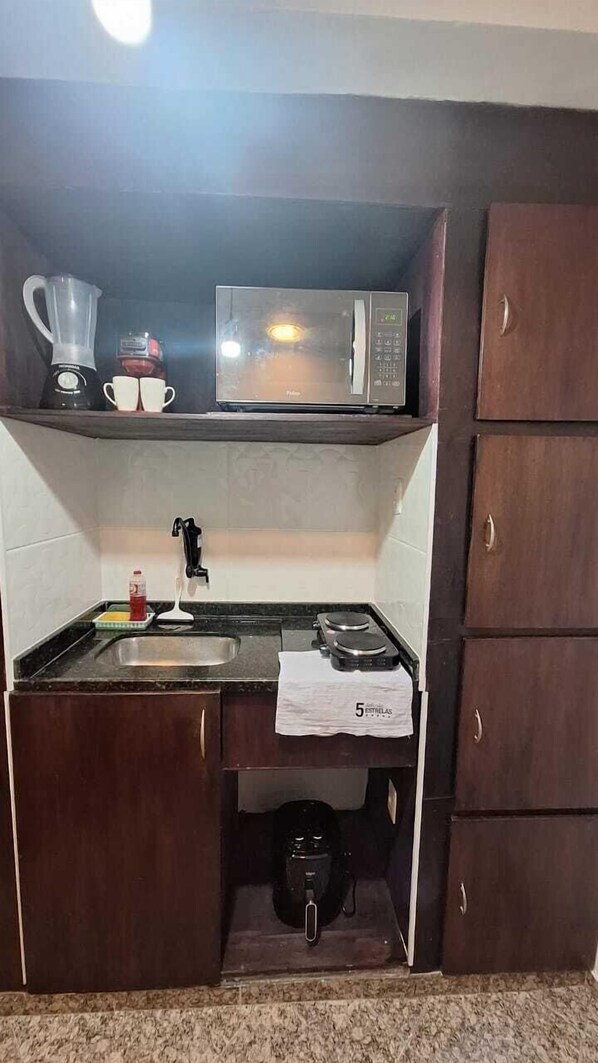 Una cocina compacta con microondas, hervidor y cafetera sobre la encimera.