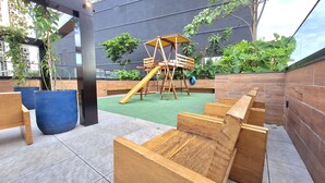 A children's play area with a wooden slide and climbing structures, surrounded by potted plants and a grey wall. - Seu aconchegante lar no centro carioca (Rio de Janeiro)