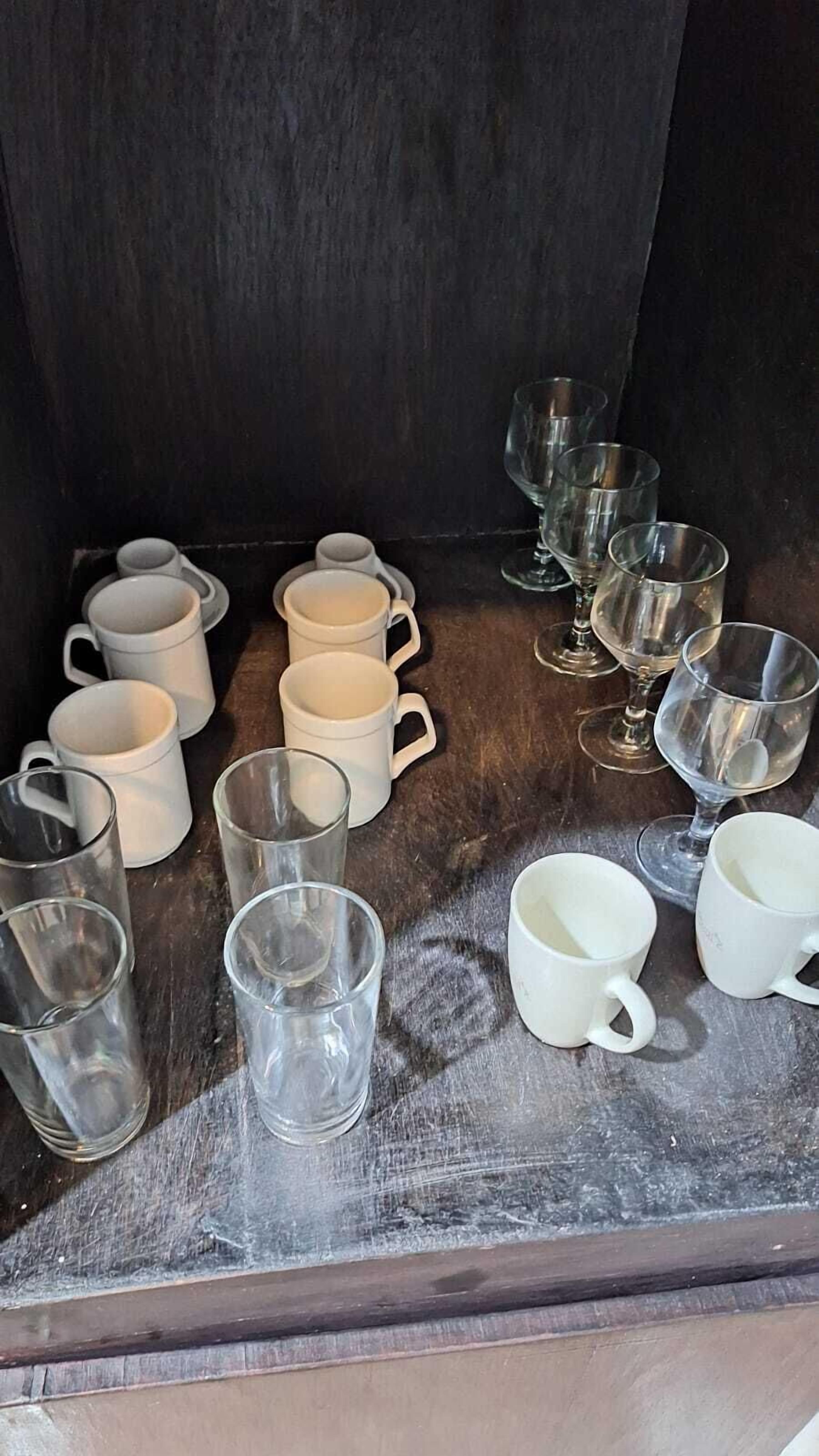Une collection de tasses en céramique blanche et de verres transparents, disposée sur une surface en bois.