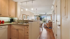 A kitchen with wooden cabinets, a sink, and a dining area with a table and chairs. - Ocean View Condo at Sea Haven (St. Augustine)