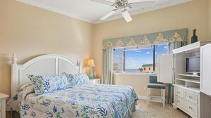 A bedroom with a bed, a TV, a desk, and a window with a view. - Ocean View Condo at Sea Haven (St. Augustine)