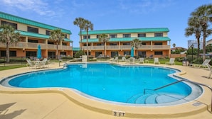 A swimming pool with lounge chairs and umbrellas, surrounded by a hotel with a green roof and multiple balconies. - Ocean View Condo at Sea Haven (St. Augustine)
