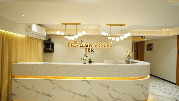 Un mostrador de recepción de hotel con encimera de mármol, un letrero que dice 'PRIVILEON HOTEL SBR' y una lámpara moderna en el techo.