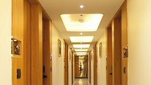 Un pasillo de hotel con puertas de madera, suelo de mármol e iluminación empotrada.