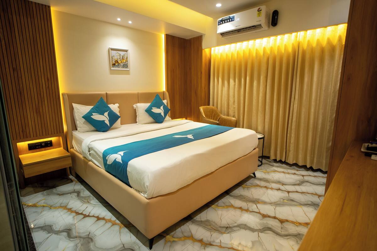 Een hotelkamer met een bed, een stoel, een nachtkastje, een wandairconditioner en een gordijn.