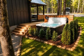 Un jacuzzi rodeado por una terraza de madera y un borde de piedra, con una pérgola de madera y un banco al fondo.