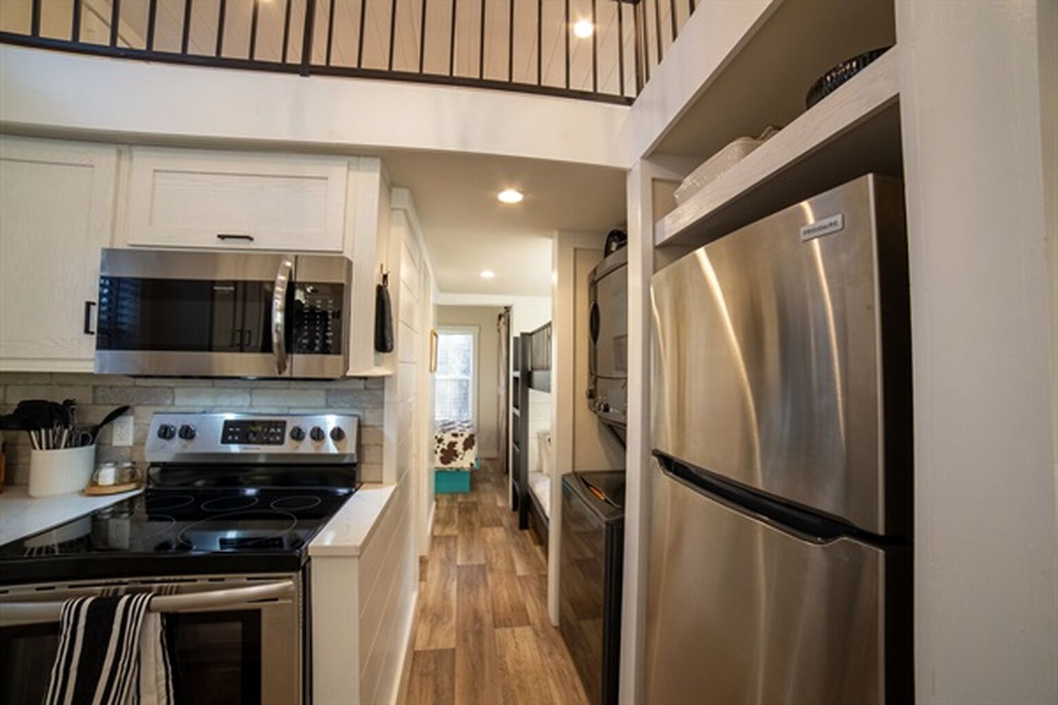 A modern kitchen with stainless steel appliances, white cabinetry, and a wooden floor.