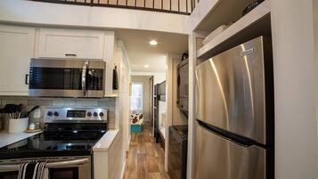 A modern kitchen with stainless steel appliances, white cabinetry, and a wooden floor.