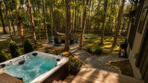 Ein Whirlpool in einem bewaldeten Garten mit einer Terrasse, Gartenmöbeln und einem Grill.