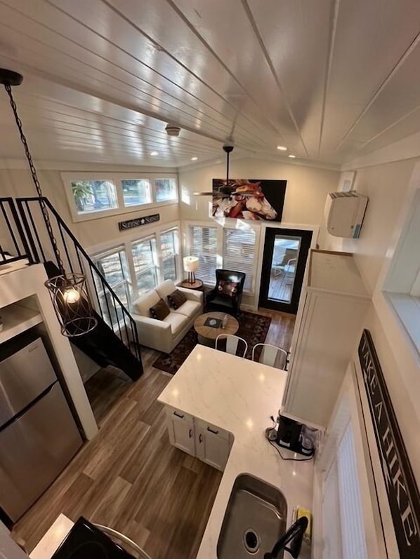 A modern kitchen with a central island, a dining area with a round table, a staircase, and a living room with a sofa and a TV.