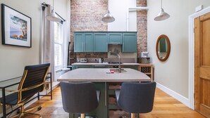 A kitchen with a brick wall, teal cabinets, and a central island with two chairs. - Charming One-Bed Oasis in Hammersmith (London)