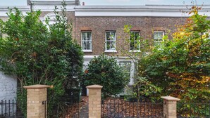 A brick townhouse with a garden, a black metal fence, and a brick pathway leading to the entrance. - Charming One-Bed Oasis in Hammersmith (London)