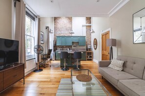 A modern living room with a TV, sofa, and a dining area with chairs and a table. - Charming One-Bed Oasis in Hammersmith (London)
