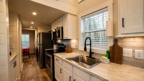 A modern kitchen with stainless steel appliances, a marble countertop, and a window with blinds.