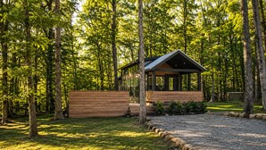 A wooden cabin with a covered porch, surrounded by a forested area.
