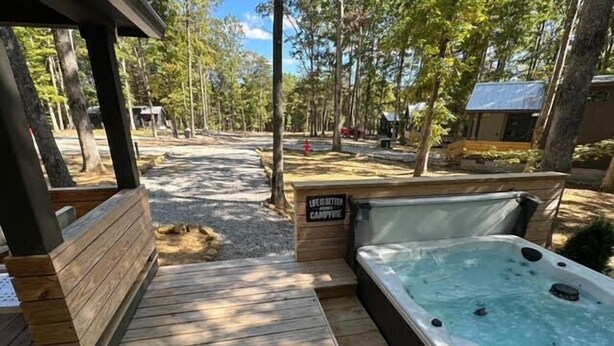 Une terrasse en bois mène à un jacuzzi, et une pancarte indique : « La vie est plus belle au coin du feu. »