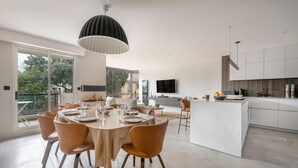 Une cuisine moderne dotée d’un îlot central, d’un coin repas avec une table ronde et des chaises, et d’une grande fenêtre offrant une vue sur l’extérieur.