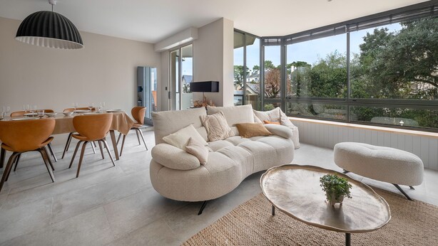 Un salon moderne comprenant un canapé, une table à manger avec des chaises et une grande fenêtre donnant sur l’extérieur.