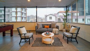 A spacious balcony with a sofa, two armchairs, a coffee table, and a foosball table. - Olive Baner by Embassy Group (Pune)