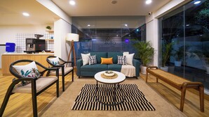 A modern living room with a sofa, chairs, a coffee table, and a view through a large window. - Olive Baner by Embassy Group (Pune)