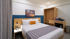 A hotel room with a bed, a nightstand, a desk with a coffee machine, and a trash bin. - Olive Baner by Embassy Group (Pune)