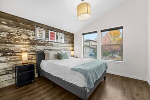 A bedroom with a bed, a wooden wall, a window, and a lamp.