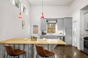 Una cocina moderna con una isla central, dos lámparas colgantes y un comedor con dos sillas.