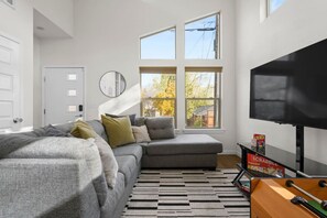 A modern living room with a sectional sofa, a flat-screen TV, and a game table.