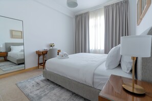 A hotel room with a bed, a desk, a chair, a mirror, and a window with curtains. - 1BR with Ocean Views Palm Jumeirah (Dubai)
