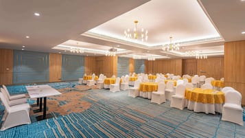 A banquet hall with rows of tables and chairs, a carpeted floor, and chandeliers.