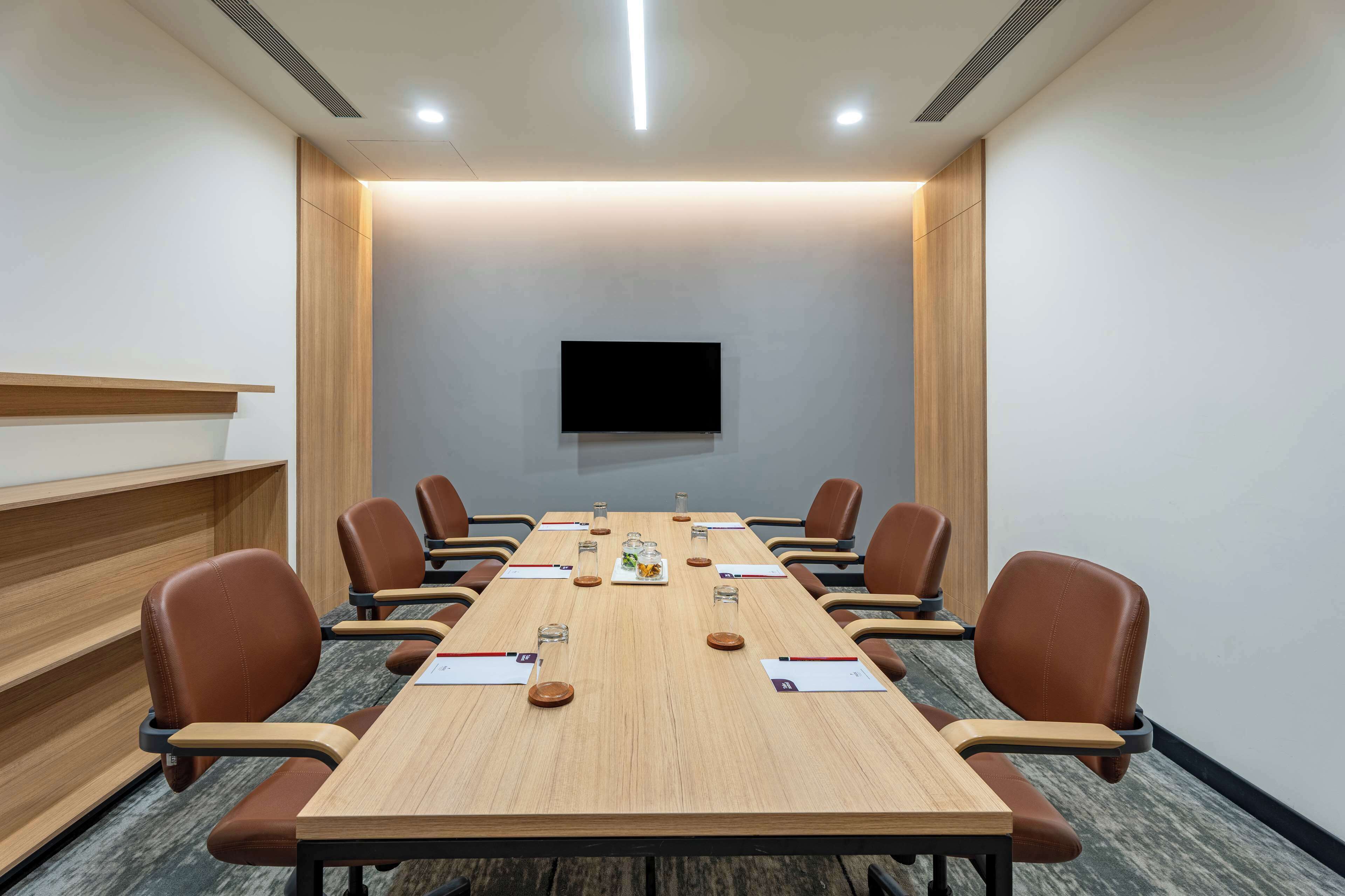 A conference room with a long table, brown chairs, a flat-screen TV, and a wooden accent wall.