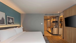 Habitació d'hotel moderna amb un llit gran, televisió, armari i petita cuina.