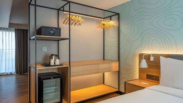A compact hotel room with a bunk bed, a minibar, a small refrigerator, a bedside table with a lamp, and a wall with a topographic design.