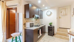 A compact kitchen with a microwave, stove, and sink. There is a small stool and a potted plant. - Pearl of Vesuvius  (Napoli)