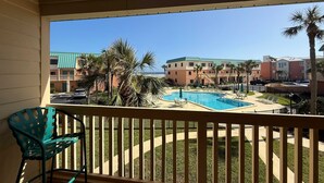 Ein Balkon mit Blick auf einen Swimmingpool, Palmen und ein mehrstöckiges Gebäude im Hintergrund.