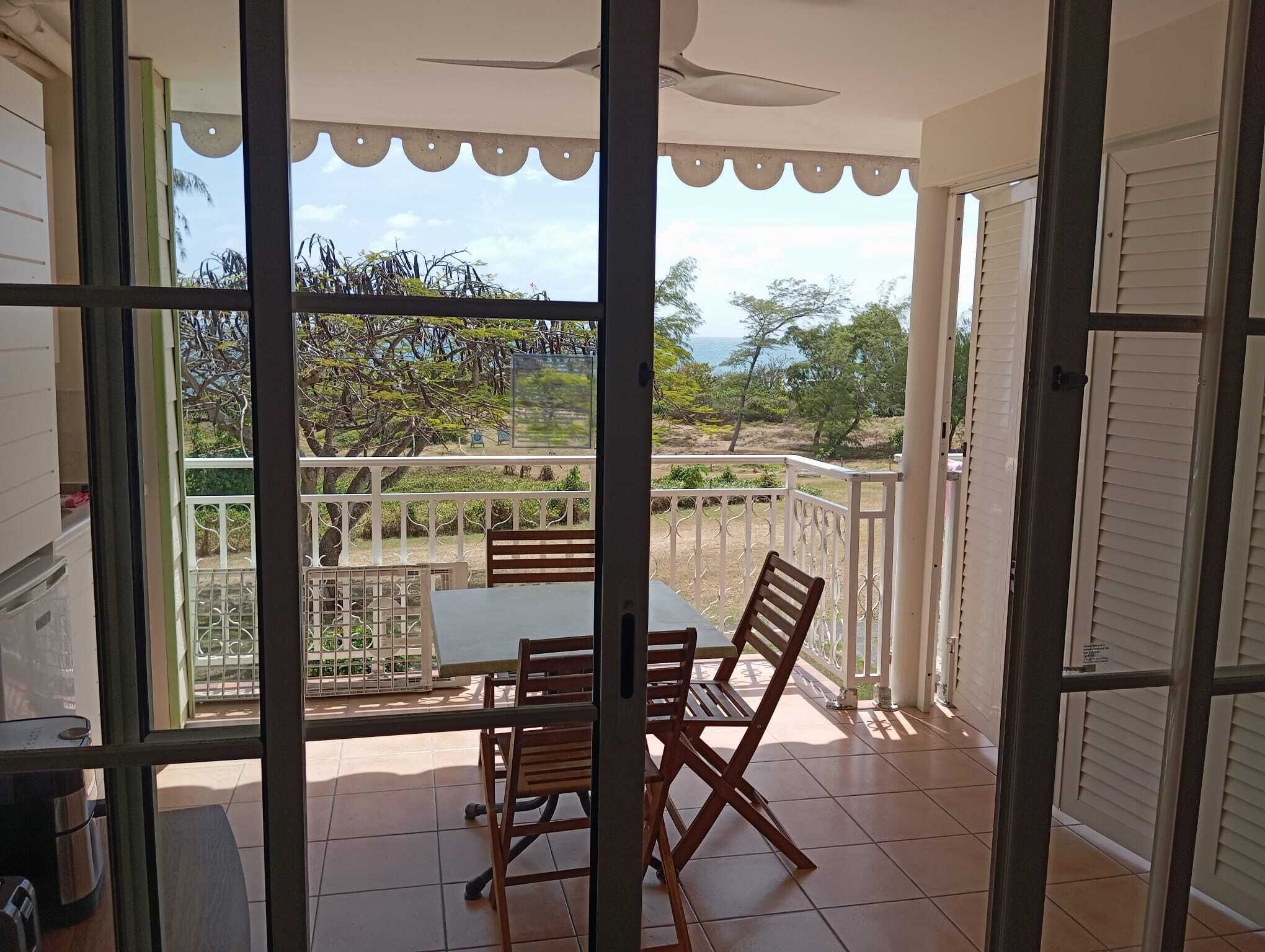A balcony with a table and chairs, a ceiling fan, and a view of the sea and trees.