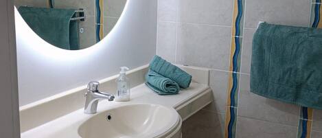 A bathroom with a round mirror, a sink, a towel rack, and a trash bin.