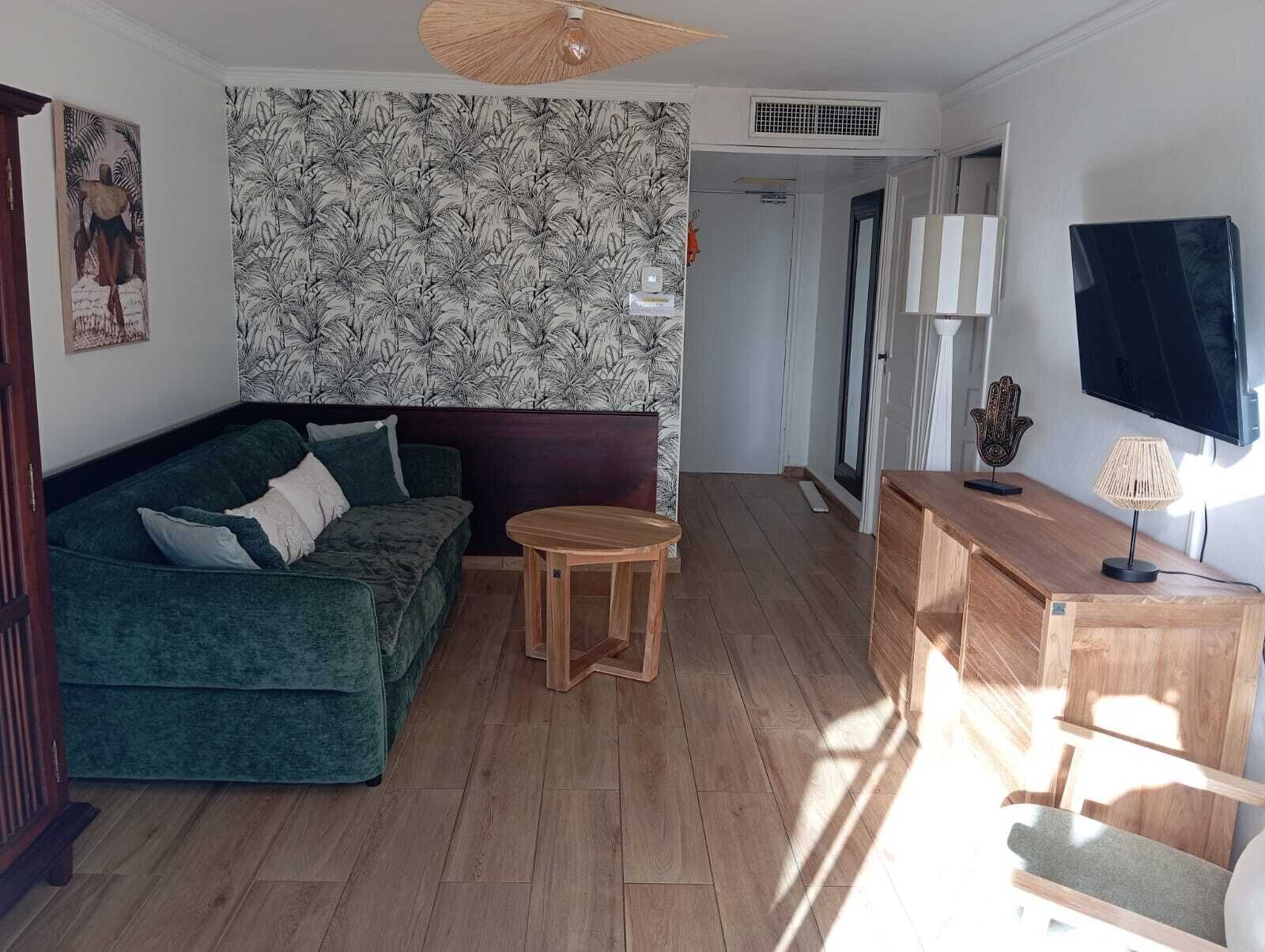A living room with a green sofa, a small wooden table, a TV, and a patterned wallpaper.