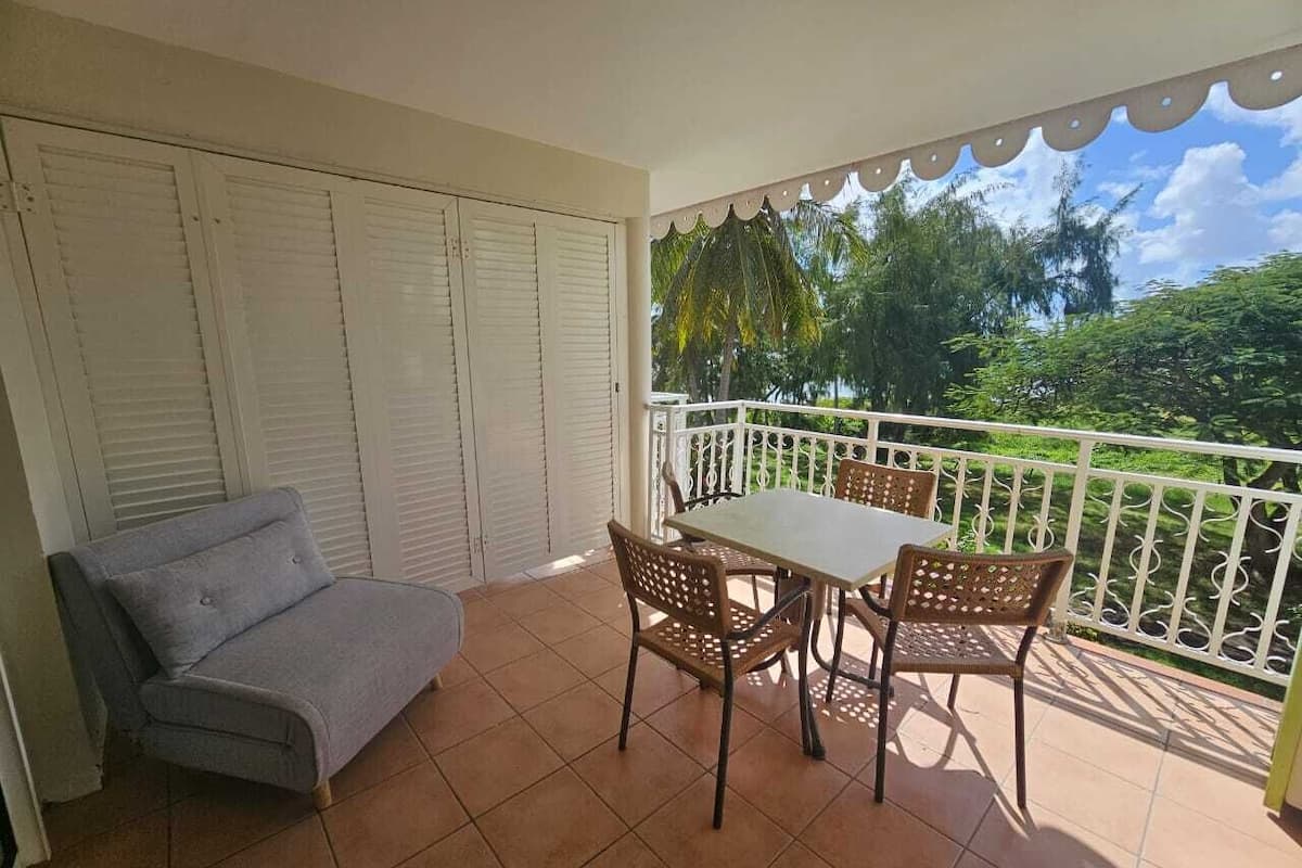 A balcony with a grey sofa and two wicker chairs, a white table, and a white railing.