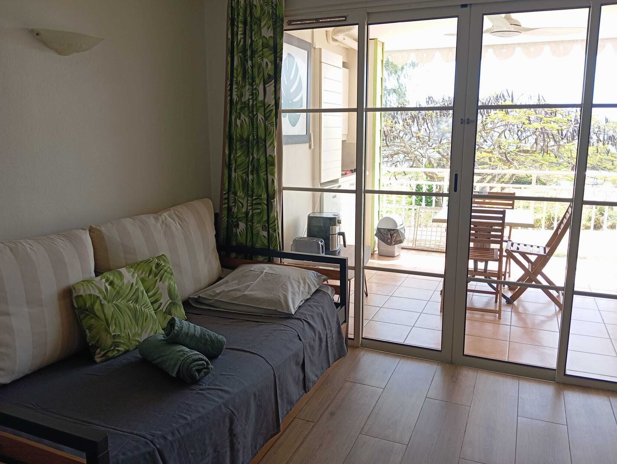 A room with a sofa, a coffee maker, and a view through a sliding glass door to an outdoor area with a table and chairs.
