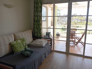 A room with a sofa, a coffee maker, and a view through a sliding glass door to an outdoor area with a table and chairs.
